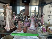 Lady figure bell prominently displayed with mini decorative plates and a pink musical snow globe in background