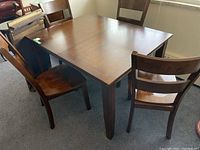 Photo showing solid wood rectangular dining table with four matching chairs around it in a room.