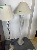Two floor lamps side by side. Left is a silver metal lamp with a tapered fabric shade, right is vintage plaster-look column lamp with a wider shade.