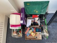 Overview of lot showing board games, landline phones, plastic bin with scissors, hole punches, cutting mats, and assorted stationery items.