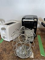 Photo showing black Keurig coffee maker, white Sunbeam toaster, and metal swivel coffee pod holder on countertop.