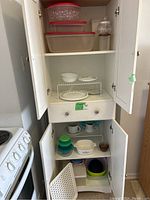 Opened kitchen cabinet showing upper and lower shelves with a variety of kitchen dishes, bowls, and plates including Corelle Cornflower dishware and plastic mixing bowls.