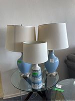 View of all three lamps on a glass round table against a white wall, showing shapes, colors, and lampshades