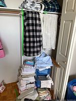 Closet with folded linens stacked including sheets, blankets, towels, and tablecloths, plus drying rack and storage drawers visible