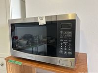 Front view of the Insignia microwave showing the control panel with cooking presets and numeric keypad, stainless steel finish on front.