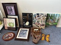 Group photo showing all items in the lot arranged against a wall and floor including framed prints, painting, wooden shelves, decorative plate, butterfly wooden decor, and mirror with candle holder
