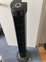 Full view of tower fan showing black and silver body and power cord coiled at base.