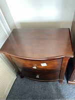 Top-front view of wooden side table showing curved front top and depth of drawers