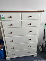 Front view of six-drawer cream-colored tallboy dresser with wooden knobs and wooden top showing some scratches and discoloration.