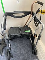 Photo of walker with padded seat, back strap, two large wheels in front, two small wheels in back, cane and grabber attached.