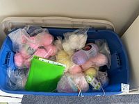 Blue plastic bin filled with assorted pastel yarn balls in plastic bags