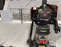 Photo shows Hoover Dual Power Max carpet cleaner upright with hose, under-cabinet metal drawer organizer, two boxed OXO toilet brush sets, and two small wooden shelves in the background on a white cloth.