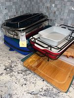 Photo shows stacked baking pans including black speckled roasting pan and white and red pans on countertop with wooden cutting boards underneath.