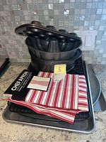 Photo showing stacked baking pans including Bundt pan, cooling racks, baking sheet, and a red and white striped chef apron still packaged