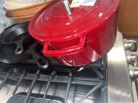 Red enameled cast iron pot with lid alongside cast iron skillets on stove