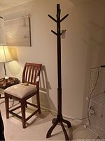 Full view of tall wooden freestanding coat holder standing next to chair and lamp.