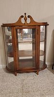 Front view of wooden curio cabinet showing glass door with brass knob and three interior shelves.
