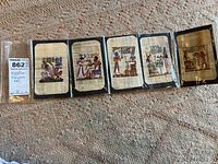 Five Egyptian papyrus art pieces in plastic sleeves, displayed side by side on carpeted floor.