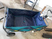Folded wagon showing blue fabric compartment and metal frame with wheels on concrete floor.