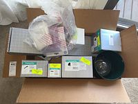 Open box showing multiple boxed and unboxed Hansgrohe faucet and shower components, plus a light fixture fixture part with glass globe.