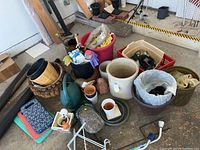 Overview of table and floor showing various plant pots, hanging baskets, kneeling pads, plant saucers, gloves, and a red bucket containing miscellaneous garden items.