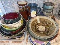 Overview of stacked pottery including bowls, plates, and platters showing varied colors and glazing.