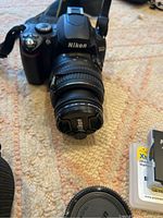 Front view of Nikon D40 with lens, lens cap attached, camera strap visible, blister pack battery