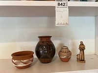 Four pottery art items on a white shelf with label 'Pottery Art'. Items include 3 vases of varying colors and designs and one small figurine.