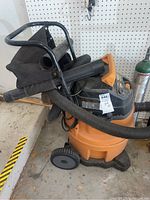 Front and angled views of a rigid professional shop vac with black hose and collection bag, showing brand and model details on top back