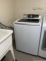 Full view of Samsung top load washer in laundry room showing machine details and surrounding area.