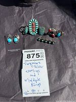 All jewelry laid out on black background: earrings, five rings, brooch