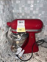 Red KitchenAid stand mixer with attached stainless steel mixing bowl and power cord on granite countertop.