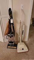 Shark and Eureka vacuum cleaners standing upright side by side on carpet.