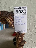 Close-up of the MaxSold tag on the mirror's frame showing vintage wall hanging mirror and measurements 35" H x 38" W