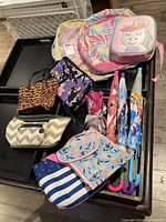 Photo showing 3 knapsacks, 2 bags, 3 lunch bags, and 4 umbrellas arranged on the floor.