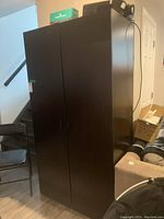 Tall black metal storage cabinet with two doors, side view showing height and adjacent items.