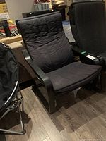 Side view of wood frame rocker chair with black quilted padded cushions in a basement setting.