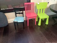 Three small chairs in a row: black wooden with blue seat, pink wooden, green plastic