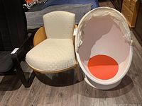 Two chairs side by side on a floor, wood frame upholstered chair with light patterned fabric and white plastic swivel chair with red cushion and canopy hood.