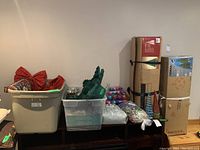 Photo of stacked boxes including Noma 3.5 foot artificial Christmas tree and other Christmas decorations such as ornaments, garland, bows, and lights stored in plastic bins