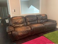 Front angle view of brown leather sofa showing three seats and reclining feature.