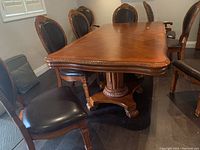Photo of wood dining table with carved edges and pedestal legs surrounded by chairs