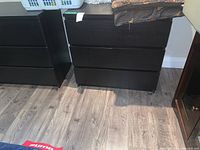 Front view of dark wood dresser with three drawers, placed on light-colored wooden floor against white wall.
