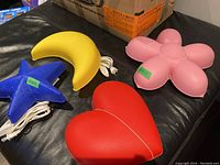 Four shaped plug-in lights shown on black surface, star, moon, heart and flower shapes with attached white cords.