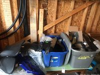 Overview of lot showing 2 plastic bins containing various black motorcycle parts, 3 motorcycle seats, and blue plastic e-bike fairings scattered around