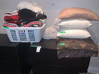 Photo showing white plastic basket containing various folded throws including crochet blanket, and piled cushions in brown, white, and patterned fabrics.