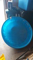 Top-down view of round blue plastic kids pool showing textured bottom surface and the pool's width, placed on a garage floor beside bins.
