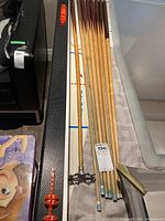 Seven wooden pool cues and one billiards bridge stick alongside a textured black cue case with red logo on the end.