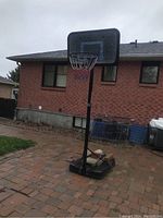Full view of Lifetime portable basketball hoop set on outdoor patio, showing black base, adjustable pole, and rectangular backboard.