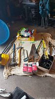 Overview of various hand tools and parts on a blanket including snow shovels, hand saws, trimmers, spirit level, pipe fittings and boxes of parts.